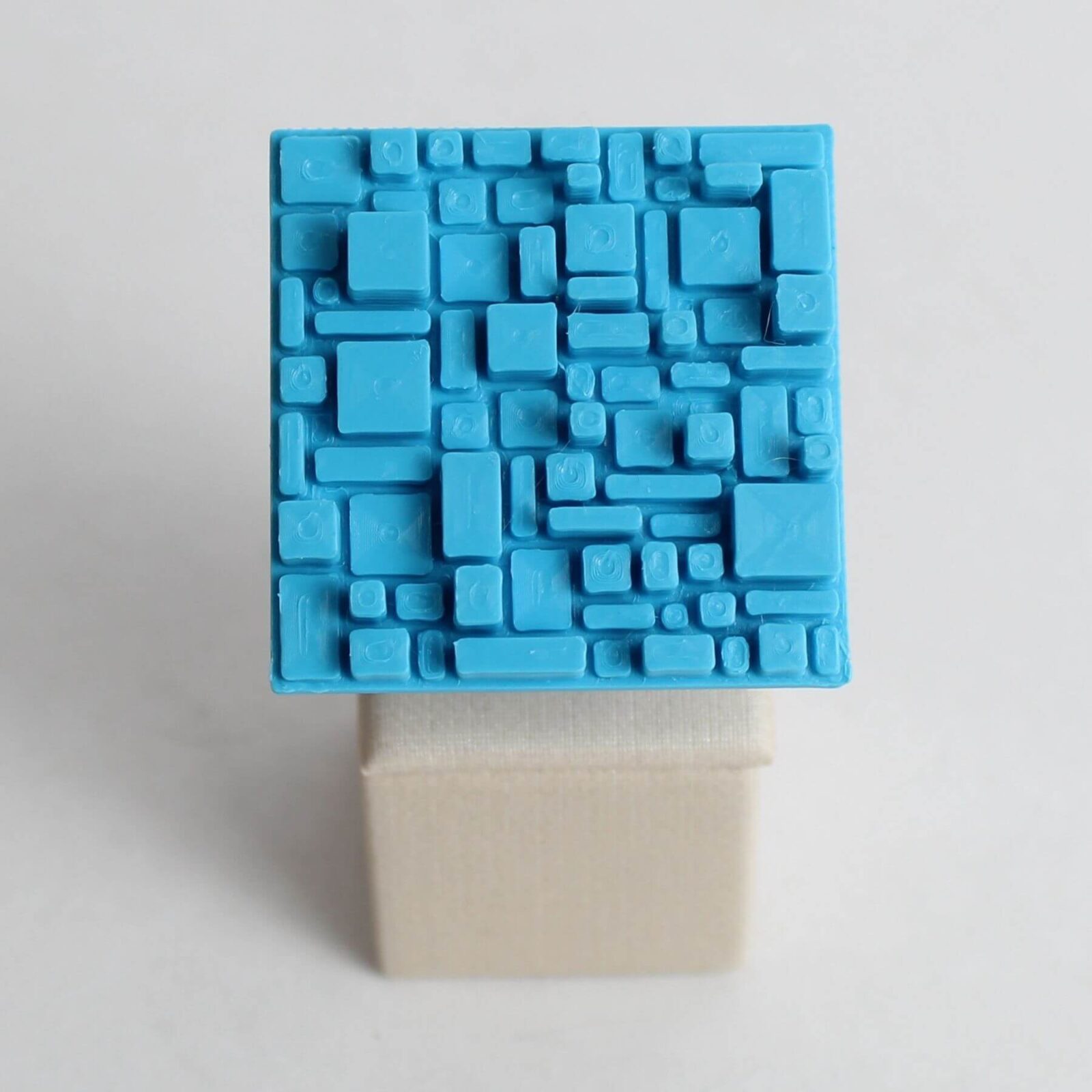 Anel quadriculado azul em PLA visto em perspectiva frontal sobre base de exposição