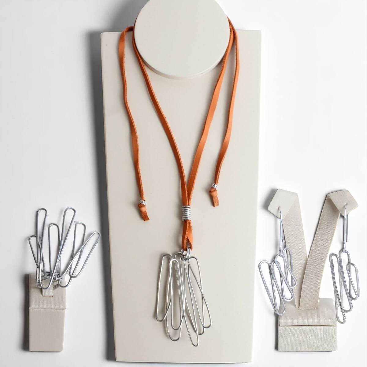 Conjunto Meteoro com colar, anel e brincos em alumínio torcido. Design moderno com couro laranja e formas esculturais.
