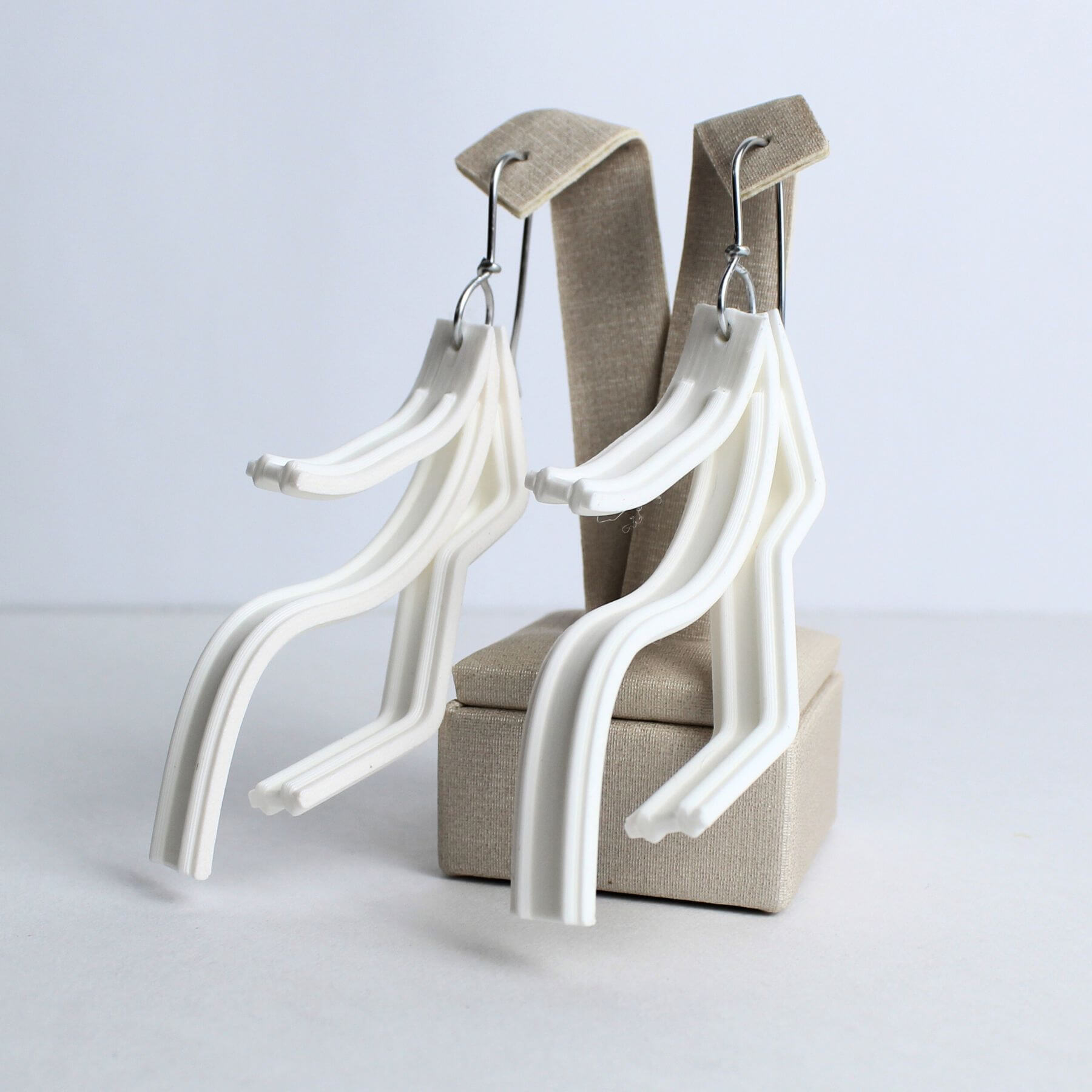 Brinco branco feito em PLA com design fluido e leveza visual, pendurado em suporte de exibição