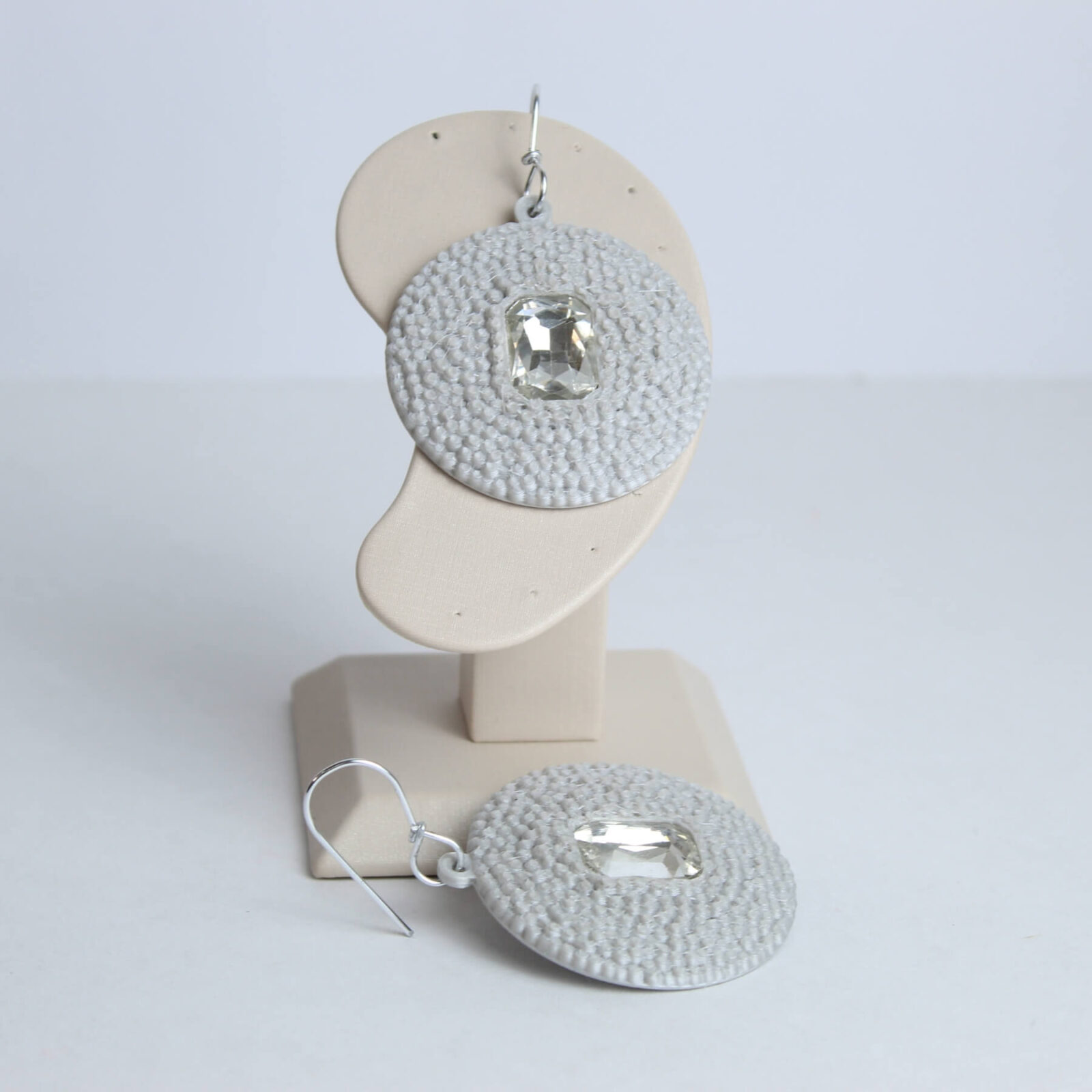 Brinco circular prateado com pedra artificial transparente em suporte de exibição