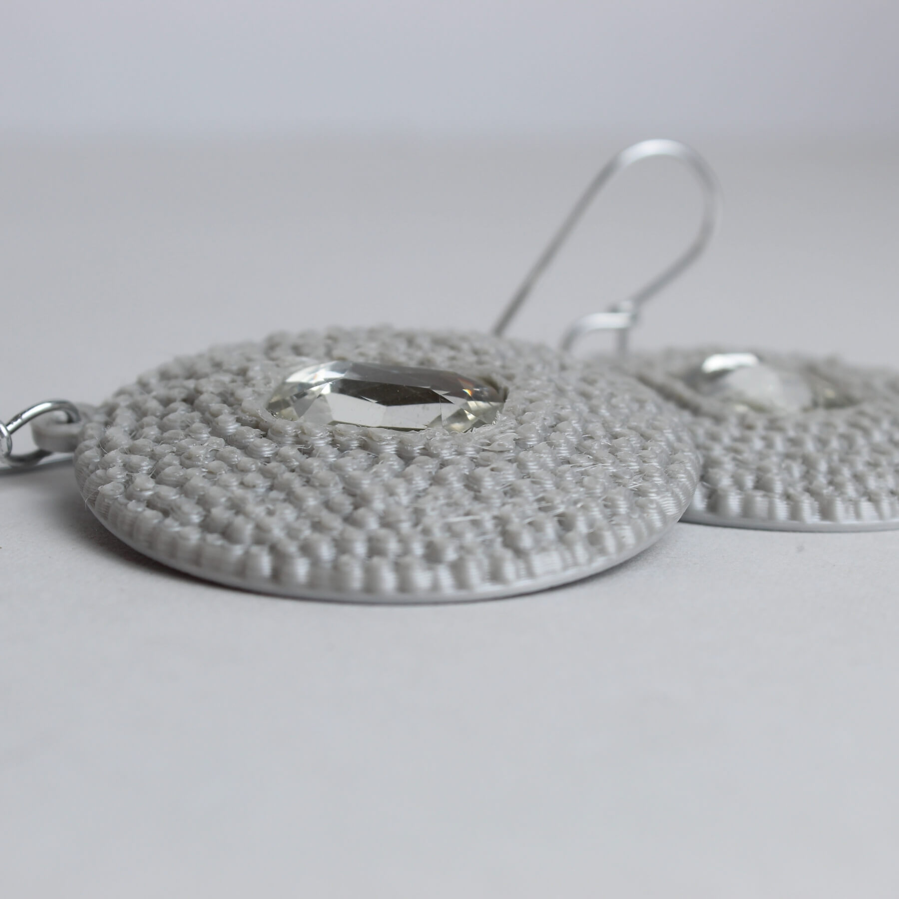 Close do brinco em PLA com textura esférica prateada e pedra transparente ao centro