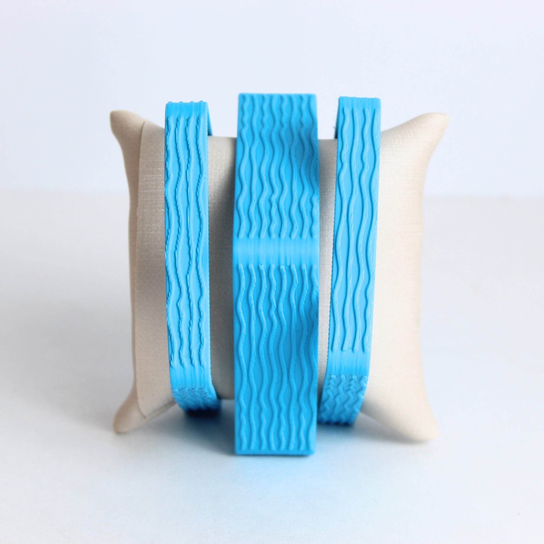 Três pulseiras azuis com textura ondulada exibidas sobre almofada clara