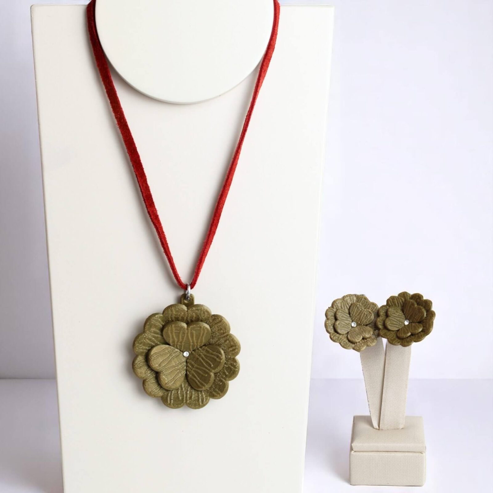 Conjunto com colar de flor verde em cordão vermelho e brincos combinando em suporte branco